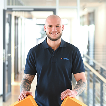 A bald man is wearing a dark blue polo shirt and is holding two orange objects in his hands.