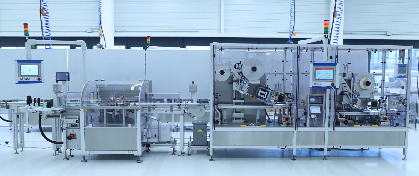 Automated production line with multiple machines, screens, and safety devices in a modern factory environment.