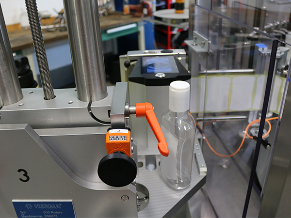 A filling machine with a transparent container and an orange lever, ready to be filled.