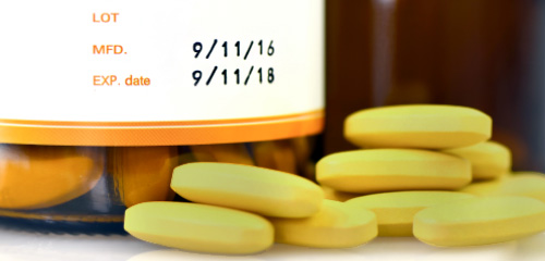 Yellow tablets are lying next to a small bottle with a label that shows the manufacturing date and the expiration date.