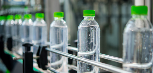 Water bottles with green caps on a conveyor belt in a production facility.