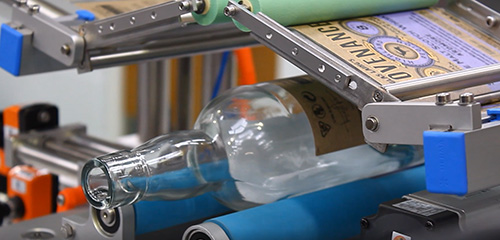 A glass bottle is being processed on a conveyor belt as it gets labeled.