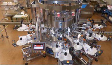 Automatic labeling machine with multiple stations, equipped with a control panel and numerous labeling arms.