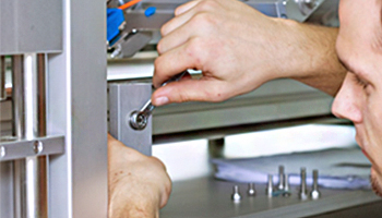 A technician tightens a screw on a metal structure with a wrench. Tools and parts are visible in the background.