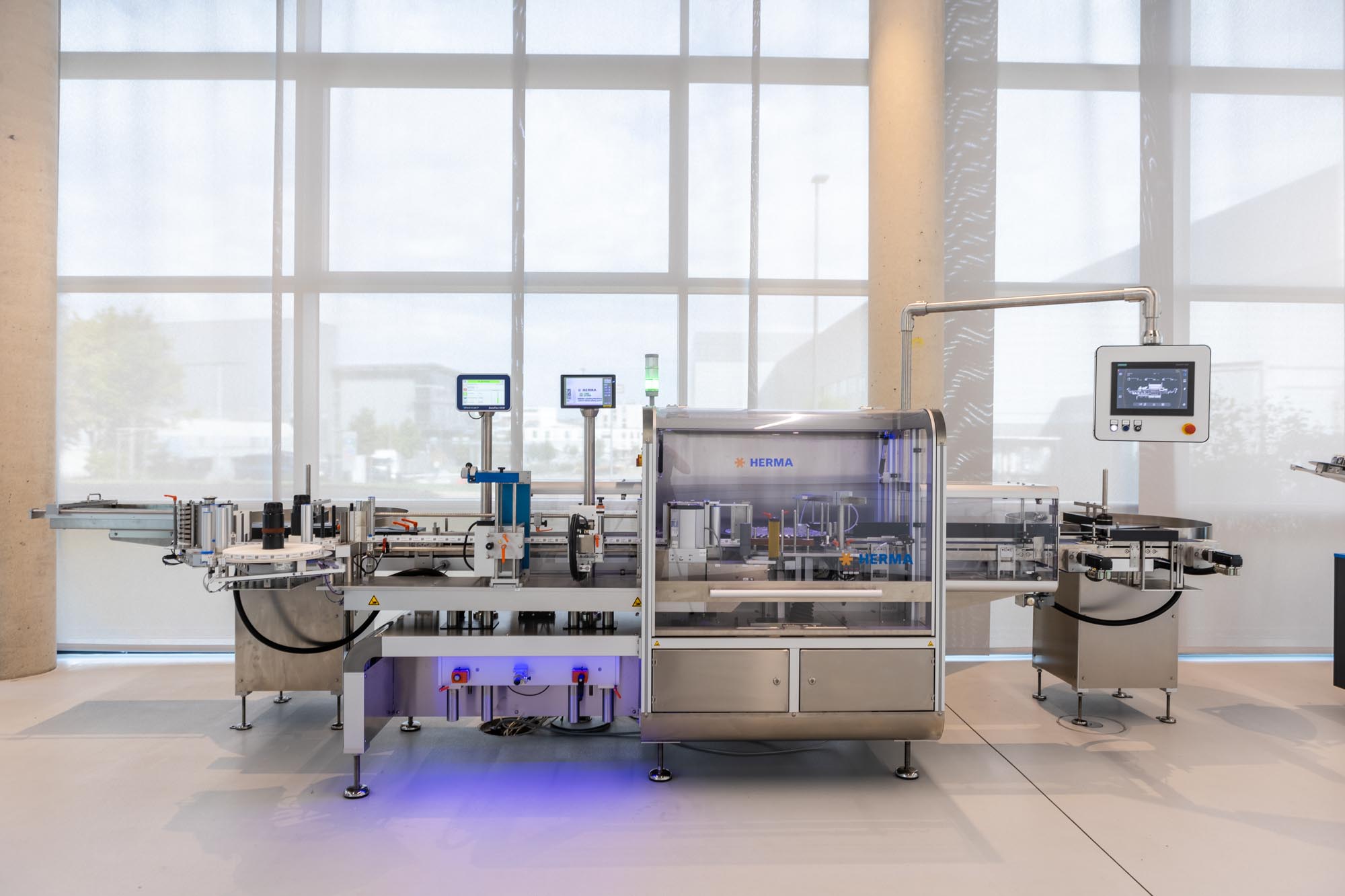 Automatic filling and labeling system in a modern production environment with multiple screens for monitoring.