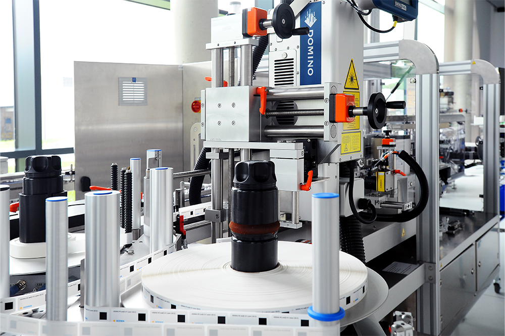 An automated packaging machine with bottles on a conveyor belt, equipped with labeling and printing systems.