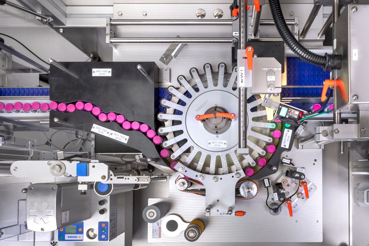 Machine for processing capsules with a rotating conveyor system and colored capsules on a conveyor belt.