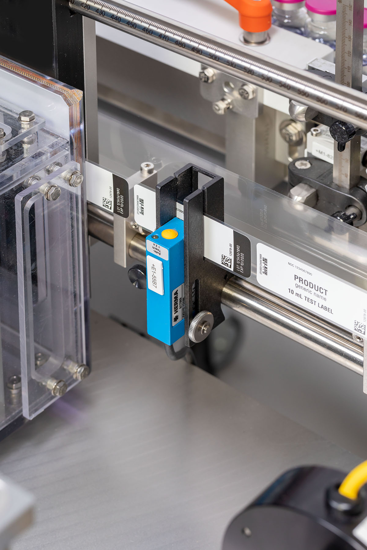 A labeling device with a blue sensor that detects labels on transparent packaging. Several labels are visible.