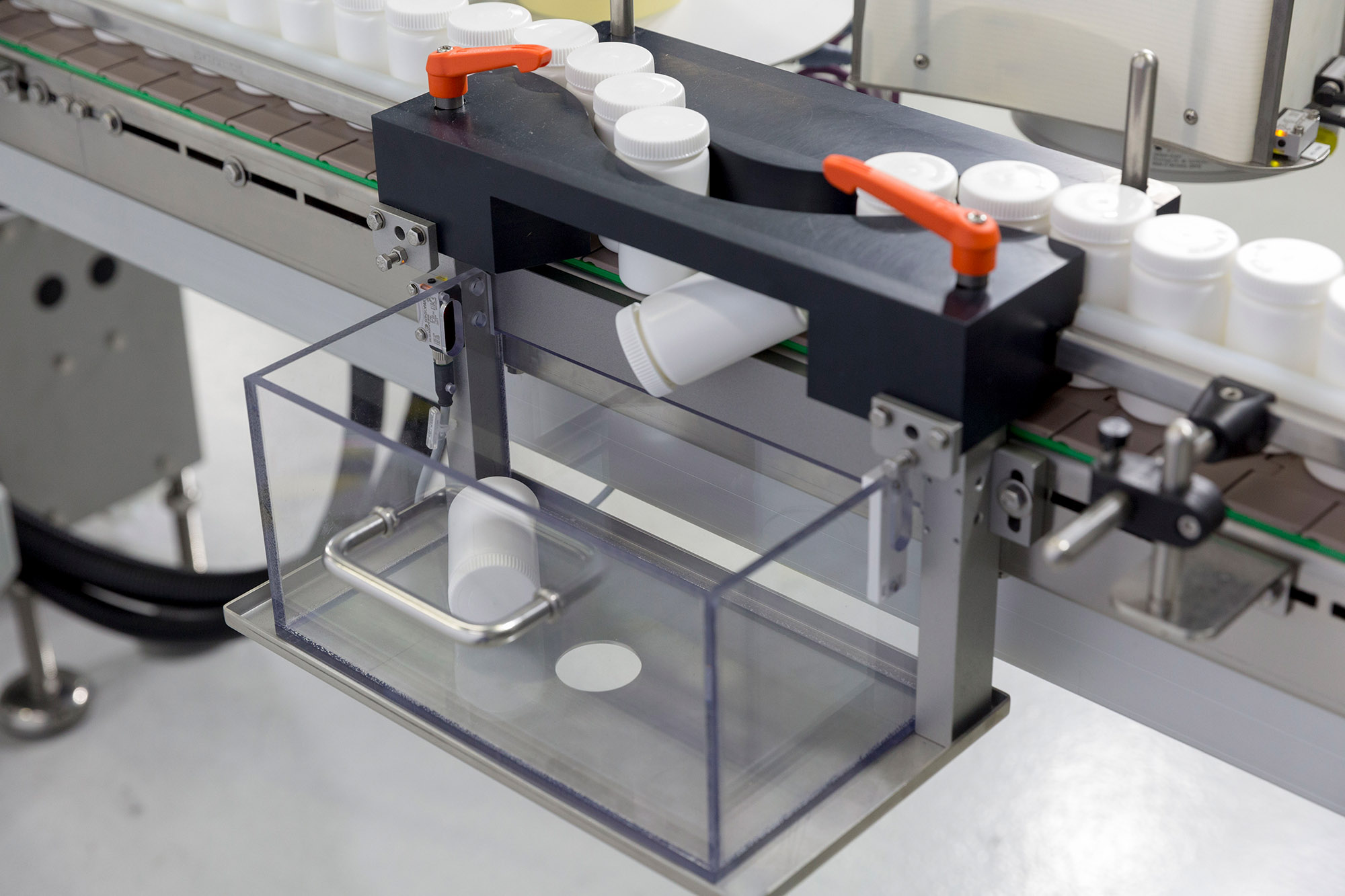 Automated packaging machine with a transparent container that picks up the container from a conveyor belt.