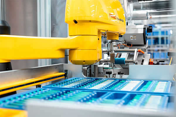 A yellow industrial robot arm is working on a conveyor belt with blue containers filled with various objects.