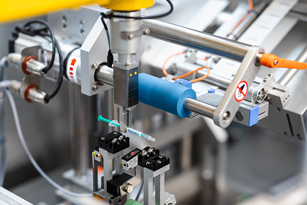 Automated machine with a robotic arm holding a syringe, surrounded by various mechanical components and sensors.