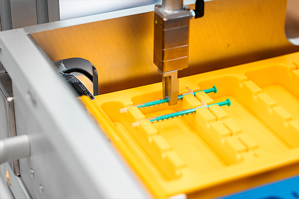 A machine places green syringes into a yellow holder designed for the storage or transport of medical devices.