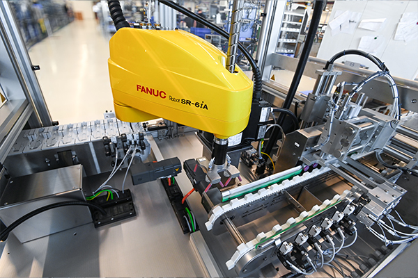 FANUC industrial robots, model R-6iA, in an automated manufacturing environment, equipped with various components for assembly.