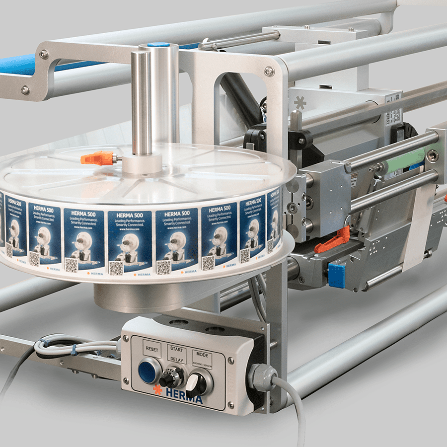 A labeling machine with a roll of labels mounted on a rotating plate and a control panel for operation.