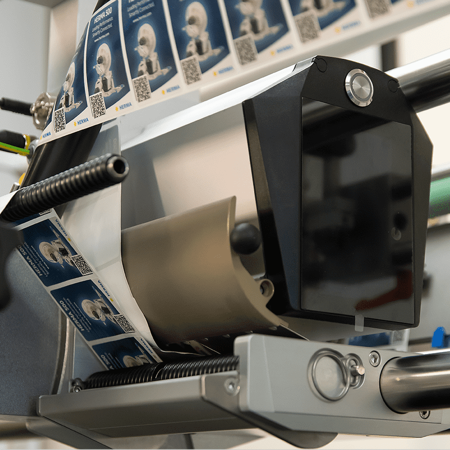A labeling machine with a roll of labels displaying QR codes and images is ready for use in a production environment.