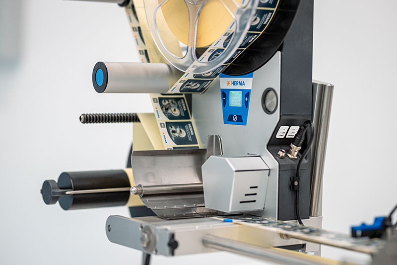 A labeling machine with rollers, control elements, and a display for adjusting the settings.