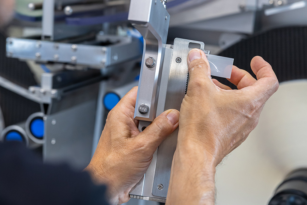 A person adjusts a precise measuring instrument with both hands while working on a technical machine.