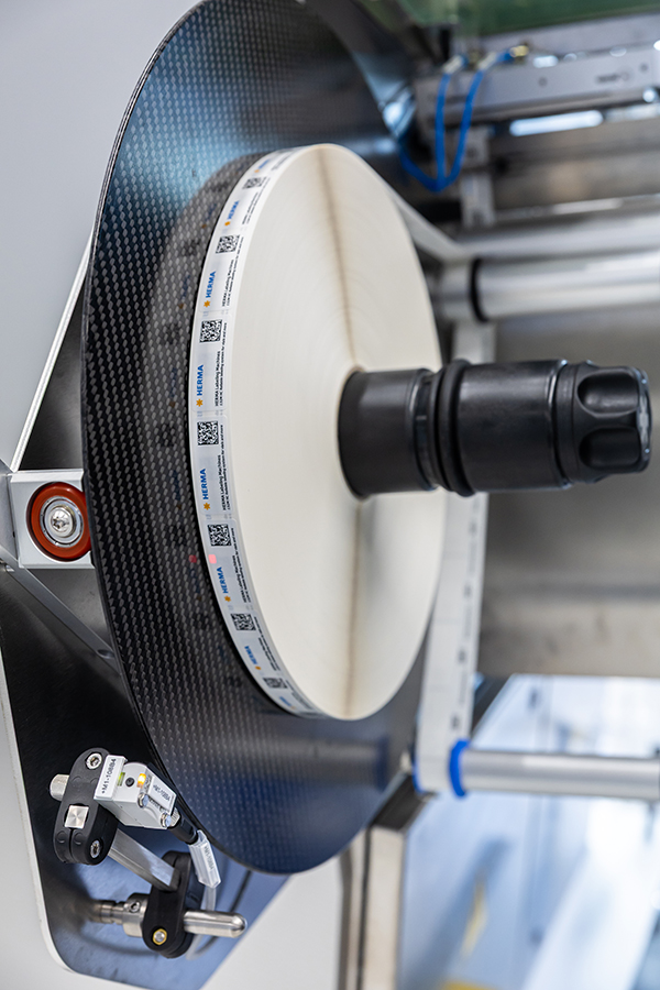 A large, round carbon roll with a central black holder, surrounded by technical components and sensors.