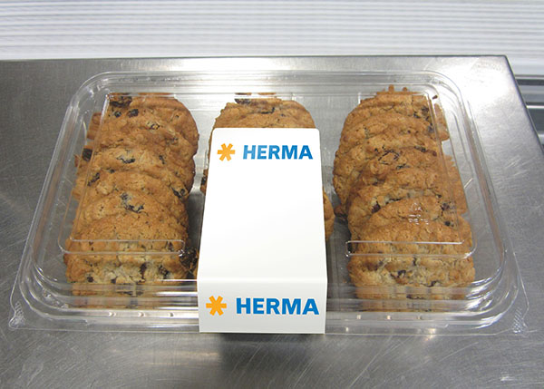 A transparent package containing several chocolate cookies, with a white label in the center that reads 'HERMA'.