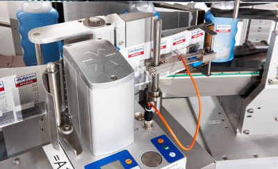 Machine for labeling bottles with precise control mechanisms and digital displays. Bottles in various colors are visible.