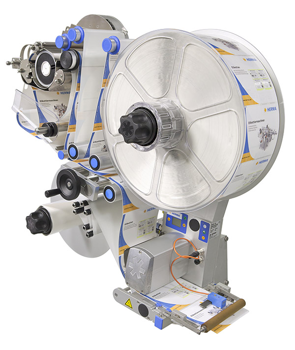 Labeling machine with a large roll of labels, various control elements, and a dispensing mechanism.