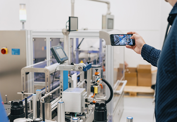 A person is holding a smartphone and filming an automated machinery setup in a production environment.