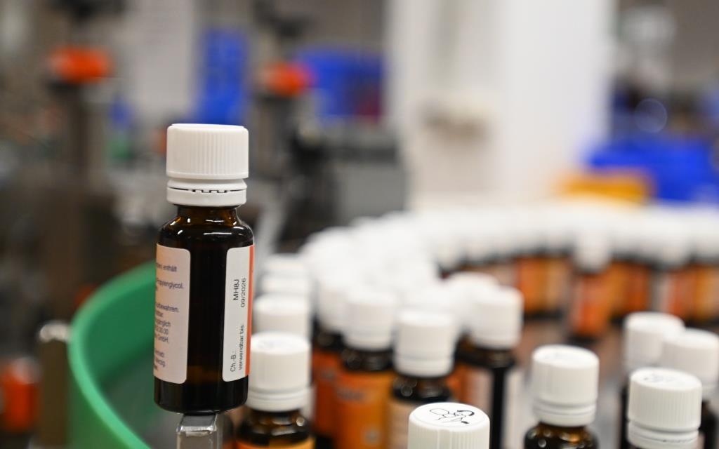 Brown bottles with white caps are lined up in a production line, with some bottles in the foreground and others in the background.