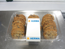 A container filled with several chocolate cookies, featuring a label in the center that says 'HERMA.