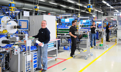 Workers in a production hall, standing by machines and workstations as they carry out various tasks.