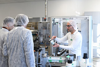 A staff member is explaining to a group of people in protective gear how to use a container in a production environment.
