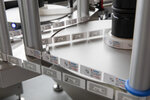 A labeling machine with multiple rollers that applies labels onto a conveyor belt surface. The labels display various information.