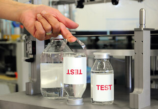 A hand lifts a label reading 'TEST' from a bottle of water, while another bottle stands beside it.