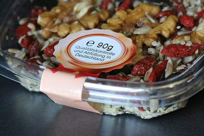 A transparent bowl filled with a mix of nuts, seeds, and dried fruits, labeled with nutritional information.