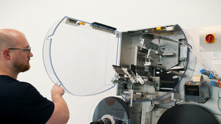 A man opens the transparent door of a machine equipped with various mechanical components.
