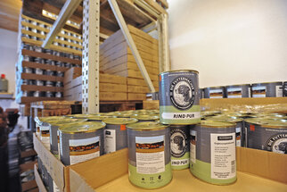 Canned beef is on a shelf in a storage room. In the background, more shelves and wooden pallets are visible.