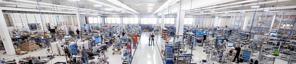 A large, modern factory hall with several workstations, machines, and employees working on various projects.