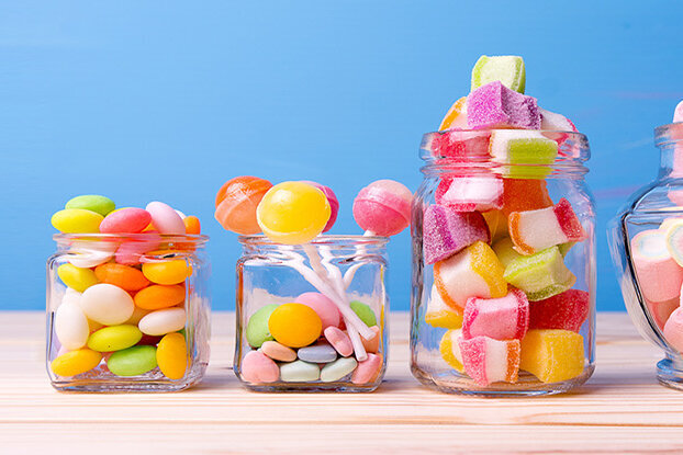 Colorful candies in various jars on a wooden surface, with a blue background.