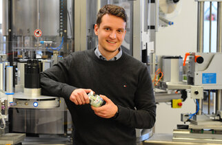 A man is holding a glass in his hand and standing next to a modern bottling machine in a production environment.