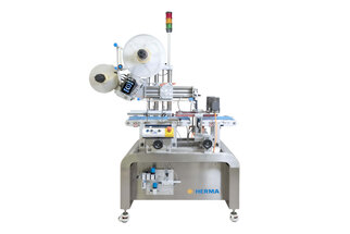 Automatic labeling machine with multiple rolls, equipped with sensors and control elements, on a sturdy table.
