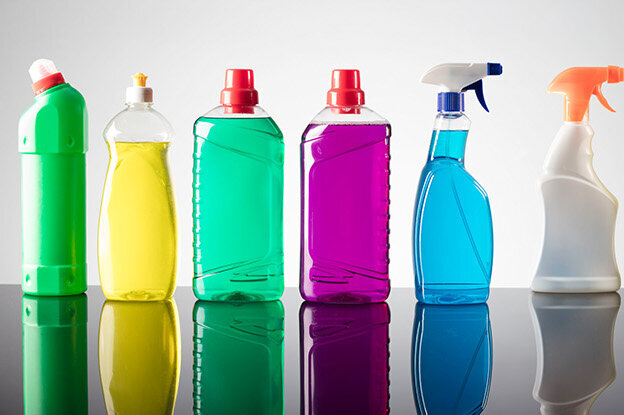 Row of cleaning product bottles in various colors on a reflective surface.