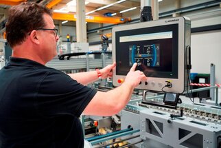A man is operating a touchscreen in a factory that displays information about machines and production data.